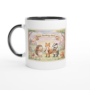 May include: White ceramic mug with a black handle and rim. The mug features a whimsical illustration of woodland creatures, including a hedgehog, fox, and badger, with the text "Bean thinking about you" on a banner.