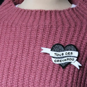 May include: A pink knitted sweater with a black heart-shaped patch that says "TOUS DES CREVARDS" in white lettering.