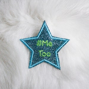 May include: A blue glitter star with a green outline and the text "#Me Too" embroidered on it.