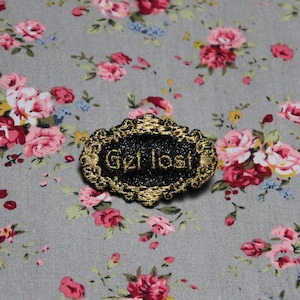 Get Lost-Juwelenbrosche „Die kostbaren, angesehenen Barockmänner“, schwarzer Paillettenstoff, bestickte Botschaft aus englischem Goldfaden, hergestellt in Frankreich
