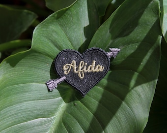 Broche Afida corazón de amor atravesado por una flecha de Cupido tela de lentejuelas negras mensaje bordado hilo de oro hecho en Francia