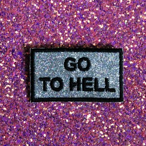 以下が含まれることがあります： 黒い文字で「GO TO HELL」と書かれた銀色のグリッターアイロン接着パッチです。