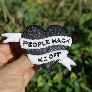 Peut inclure: Écusson en forme de cœur noir pailleté avec une bannière blanche portant l'inscription "PEOPLE HACK ME OFF" en noir. Le patch est une broderie, adapté aux vêtements ou accessoires.