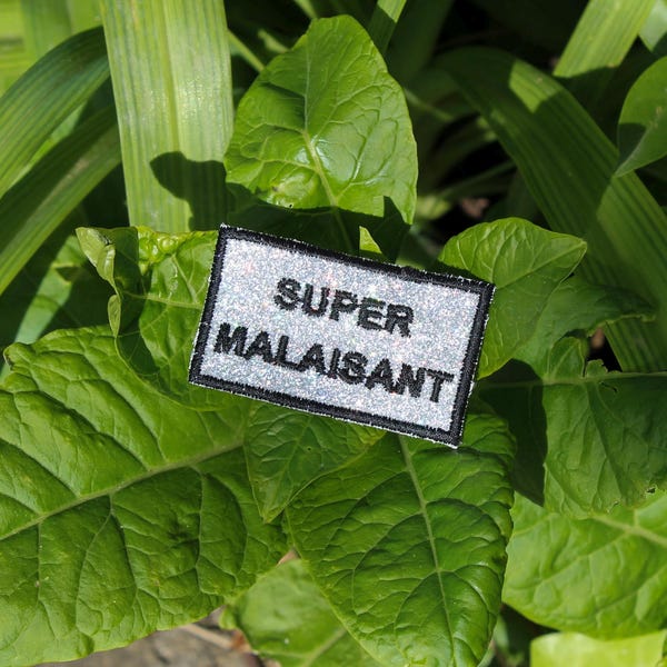 SUPER UNCOMFORTABLE brooch in silver fabric with sparkling sequins and rainbow highlights, embroidered message in French with a black outline, made in France