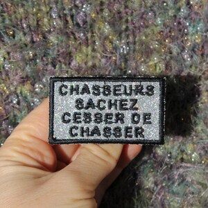 Puede incluir: Un parche bordado en plata y negro con el texto "CHASSEURS & ACHEZ CESSER DE CHASSER".