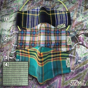 Puede incluir: Tres mascarillas de tela a cuadros con lazos el&aacute;sticos para las orejas. Las mascarillas est&aacute;n superpuestas. La mascarilla superior es negra, verde y blanca. La mascarilla del medio es blanca, roja y verde. La mascarilla inferior es turquesa, amarilla y verde. Cada mascarilla tiene una etiqueta verde con el texto "SZMIC" en ella.