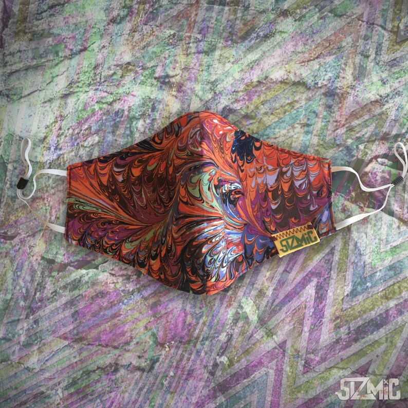 Puede incluir: Una mascarilla facial con un patr&oacute;n de m&aacute;rmol colorido en tonos naranja, rojo, morado y azul. La mascarilla tiene cintas el&aacute;sticas blancas y una peque&ntilde;a etiqueta amarilla con el texto "www.stzmic.com" en ella.