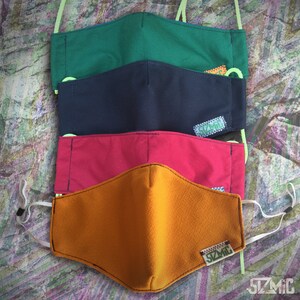 Puede incluir: Cuatro mascarillas de tela en diferentes colores: verde, azul marino, rojo y naranja. Cada mascarilla tiene un peque&ntilde;o logotipo con el texto "SZMIC" en &eacute;l.