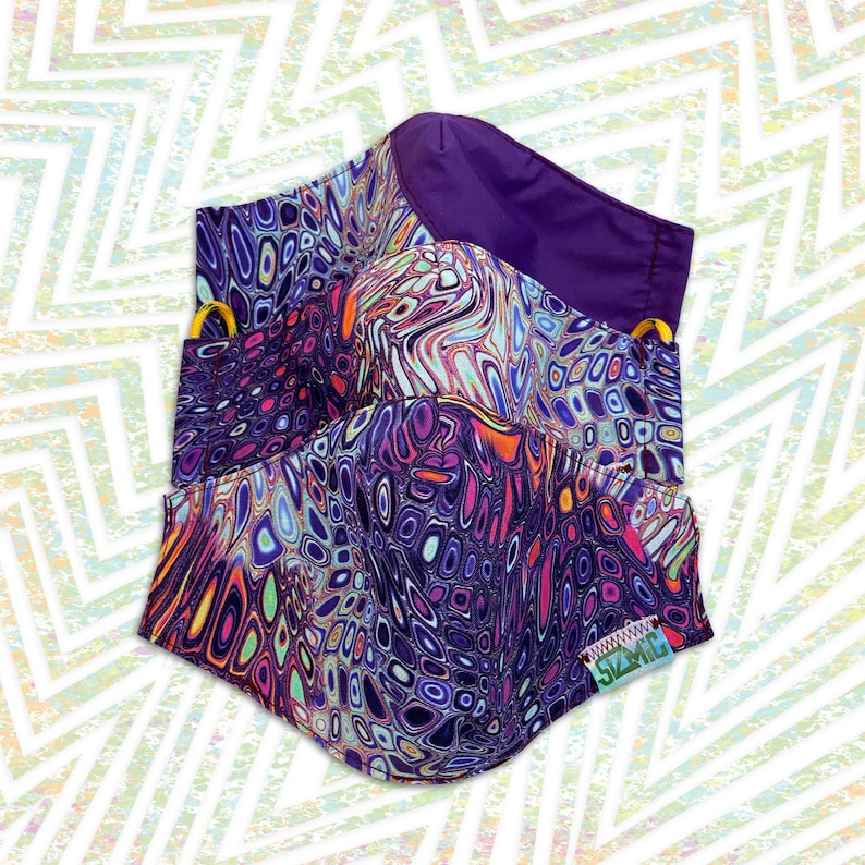 Puede incluir: Dos mascarillas con un patr&oacute;n abstracto de espiral en morado, rosa, azul y amarillo. Las mascarillas est&aacute;n hechas de tela y tienen una etiqueta cosida que dice "SZMC".