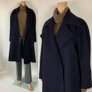 May include: A navy blue wool coat with a wide lapel collar. The coat is double-breasted and reaches to the ankles. The mannequin is also wearing a brown turtleneck sweater and gray pants. The coat is displayed on a mannequin.