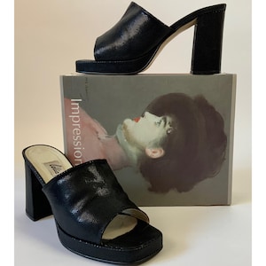 May include: Two black platform sandals with open toes and block heels. The sandals are made of a textured material and are displayed on a book titled "Impression". The heels appear to be approximately 4 inches high.