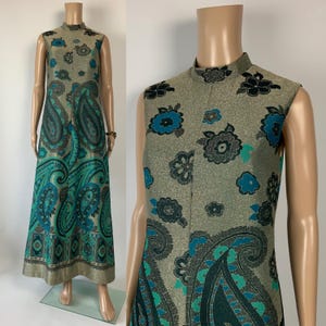 Może przedstawiać: Bezrękawnikowa, długa suknia z wysokim dekoltem. Sukienka ma złote tło z wzorem paisley i kwiatowym w kolorze turkusowym, czarnym i szarym. Dół jest wykończony złotą lamówką.