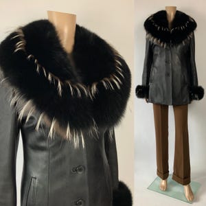 May include: Black leather jacket with a large fur collar and fur cuffs. The jacket has a button-up front and is paired with brown pants. The fur trim has black, white, and tan accents. The jacket is displayed on a mannequin.