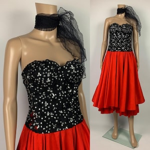 May include: A strapless black sequined bodice dress with a red skirt. The bodice is covered in silver sequins. A black choker and sheer scarf are draped around the neck. The dress is displayed on a mannequin.