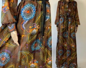 May include: A long-sleeved brown maxi dress featuring a vibrant floral and paisley pattern in shades of blue, orange, and white. The dress includes a collared neckline, button-down front, and a thin black rope belt with gold-toned metal accents.