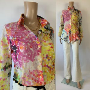 Könnte beinhalten: Ein Button-Down-Hemd mit einem lebendigen Blumenmuster in Pink, Gelb, Orange und Lila. Das langärmlige Hemd wird mit einer weißen Hose kombiniert. Das Hemd wird auf einer Schaufensterpuppe präsentiert.
