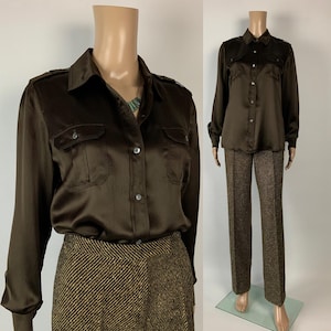 May include: A brown satin button-down shirt with two chest pockets and long sleeves. The shirt is paired with brown tweed pants. The outfit is displayed on a mannequin.