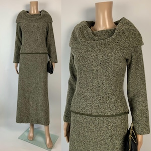 Op de afbeelding: Een tweedelig olijfgroen gebreid setje op een mannequin. De set bestaat uit een top met lange mouwen en een col en een bijpassende lange rok. Een kleine zwarte clutch wordt vastgehouden. De stof heeft een gespikkelde textuur.