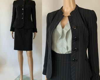 Peut inclure: Ensemble jupe noir à fines rayures sur mannequin. La veste ajustée a un col rond et une fermeture boutonnée, associée à une jupe crayon assortie. La veste a un détail basque. L'ensemble est présenté sur un mannequin.