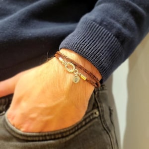 May include: A brown leather bracelet with a horseshoe charm and a small round charm with the letter "F" engraved on it.