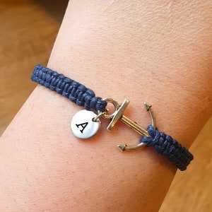 Peut inclure: Un bracelet tressé bleu marine avec un charme d'ancre argenté et un charme de disque argenté avec la lettre 'A' dessus.