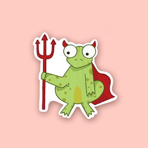 May include: A sticker featuring a cartoon frog with devil horns and a red cape, holding a red trident. The frog is green with yellow spots and large, googly eyes. The sticker has a white border and is set against a pink background.
