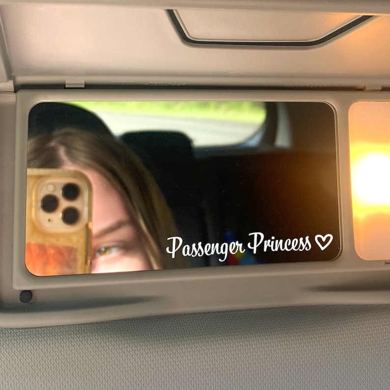 May include: A rearview mirror in a car with a sticker that says "Passenger Princess" with a heart symbol.