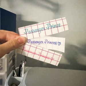 May include: Three white labels with red grid lines and blue and pink text. The top label reads "Passenger Prince". The middle label reads "Passenger Princess" with a pink heart. The bottom label reads "Passenger Princess" with a pink heart.