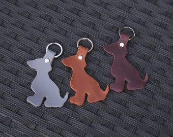 May include: Three dog-shaped keychains made of leather in gray, tan, and dark brown. Each keychain features a silver-toned metal ring attached to the top with a small silver rivet, showcasing a simple silhouette of a seated dog in three distinct colors.