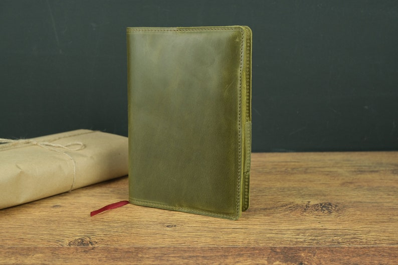 May include: A green leather journal with a red ribbon bookmark. The journal has a stitched edge and a textured surface.