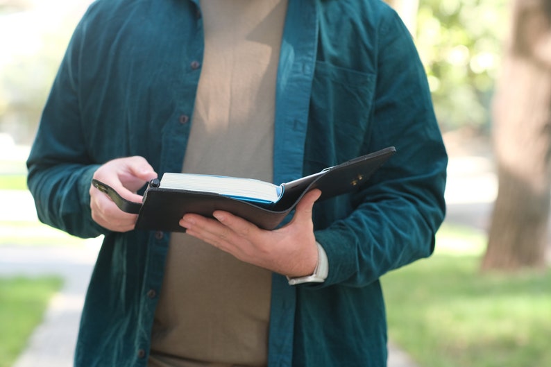 May include: A person holding a black leather bound journal with a blue pen in their hand.