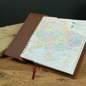 May include: A brown leather-bound journal with a map of Ukraine open inside. The map shows the different regions of the country. The journal has a red ribbon bookmark.