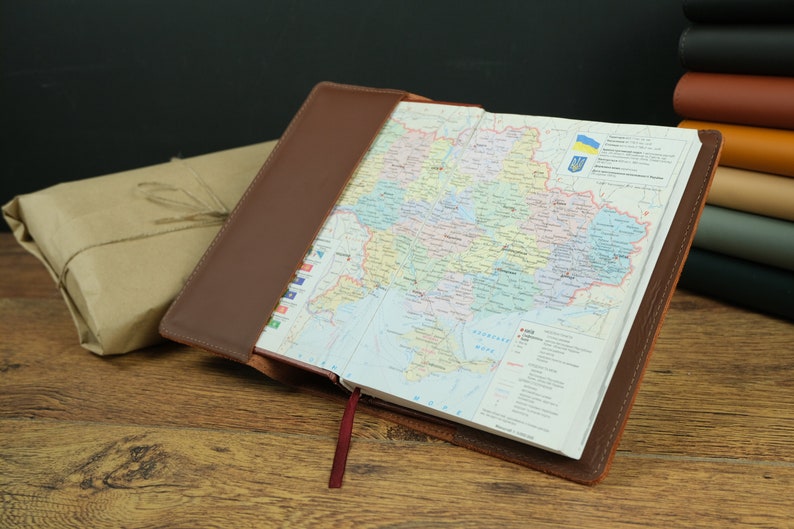 May include: A brown leather-bound journal with a map of Ukraine open inside. The map shows the different regions of the country. The journal has a red ribbon bookmark.