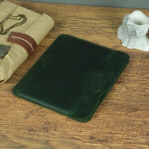 Puede incluir: Una funda de cuero verde bosque oscuro con un acabado mate suave y esquinas redondeadas. El estuche protector rectangular presenta costuras visibles a lo largo de los bordes y un perfil delgado y plano diseñado para guardar una tableta o dispositivo.
