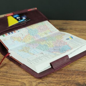 May include: A burgundy leather journal cover with a map of Ukraine inside. The cover has a pocket on the front for cards and a red ribbon bookmark.
