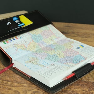 May include: A black leather journal with a red ribbon bookmark. The journal is open to a page with a map of Ukraine. A pen is tucked into the journal's cover.