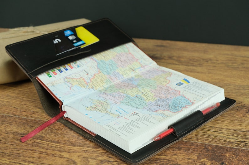 May include: A black leather journal with a red ribbon bookmark. The journal is open to a page with a map of Ukraine. A pen is tucked into the journal's cover.