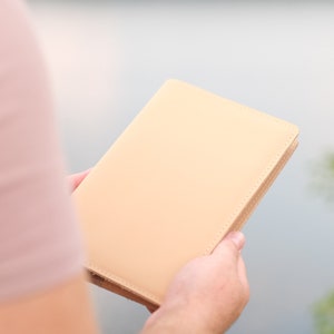 May include: A person holding a light beige leather bound journal.