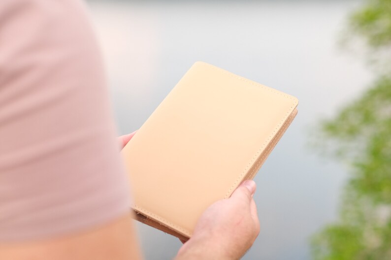 May include: A person holding a light beige leather bound journal.