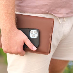 May include: A brown leather phone case with a black phone inside. The phone has a camera with multiple lenses.