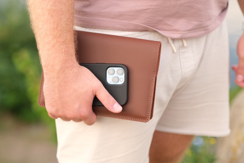 May include: A brown leather phone case with a black phone inside. The phone has a camera with multiple lenses.