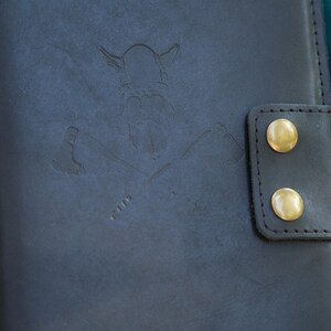 May include: A black leather journal with a brass embossed Viking design and two brass snap closures.