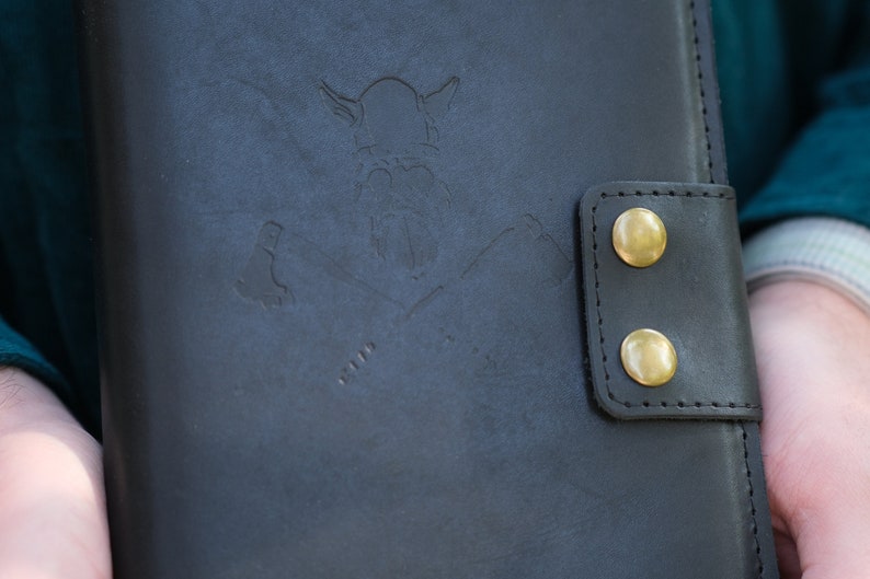 May include: A black leather journal with a brass embossed Viking design and two brass snap closures.