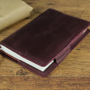 May include: A burgundy leather notebook cover with a white notebook inside. The cover has a flap that closes with a button.