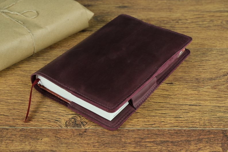 May include: A burgundy leather notebook cover with a white notebook inside. The cover has a flap that closes with a button.