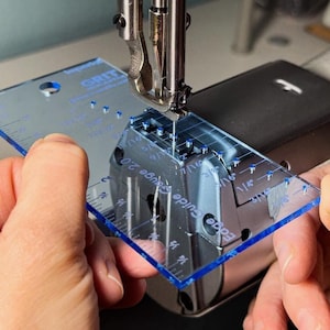 May include: A clear blue plastic sewing guide with markings in inches and a "Guide 2.0" label. The guide is being held in front of a sewing machine needle.