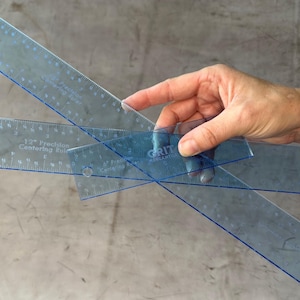May include: Three clear plastic rulers with blue markings. The rulers are labeled "12" Precision Centering Ruler" and "GRIT Mercantile Co."