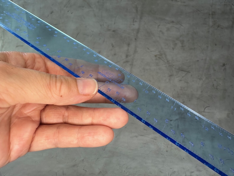 May include: A clear blue plastic ruler with black markings. The ruler is 12 inches long and has markings for every 1/16th of an inch.