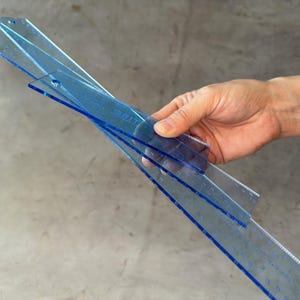 May include: Three blue plastic rulers stacked together. The rulers are marked with measurements in inches.