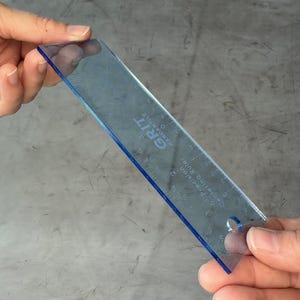 May include: A clear blue plastic ruler with the text "GRIT" and "Precision Quilting Ruler" printed on it. The ruler has markings in inches and is 12 inches long.